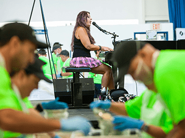 Female singer and group of people volunteering at Oshkosh Corporation's Feed the Body, Feed the Soul event