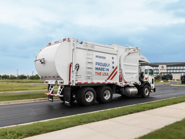 White McNeilus front loader refuse and recycling truck with red, white and blue graphics driving in front of Oshkosh global headquarters