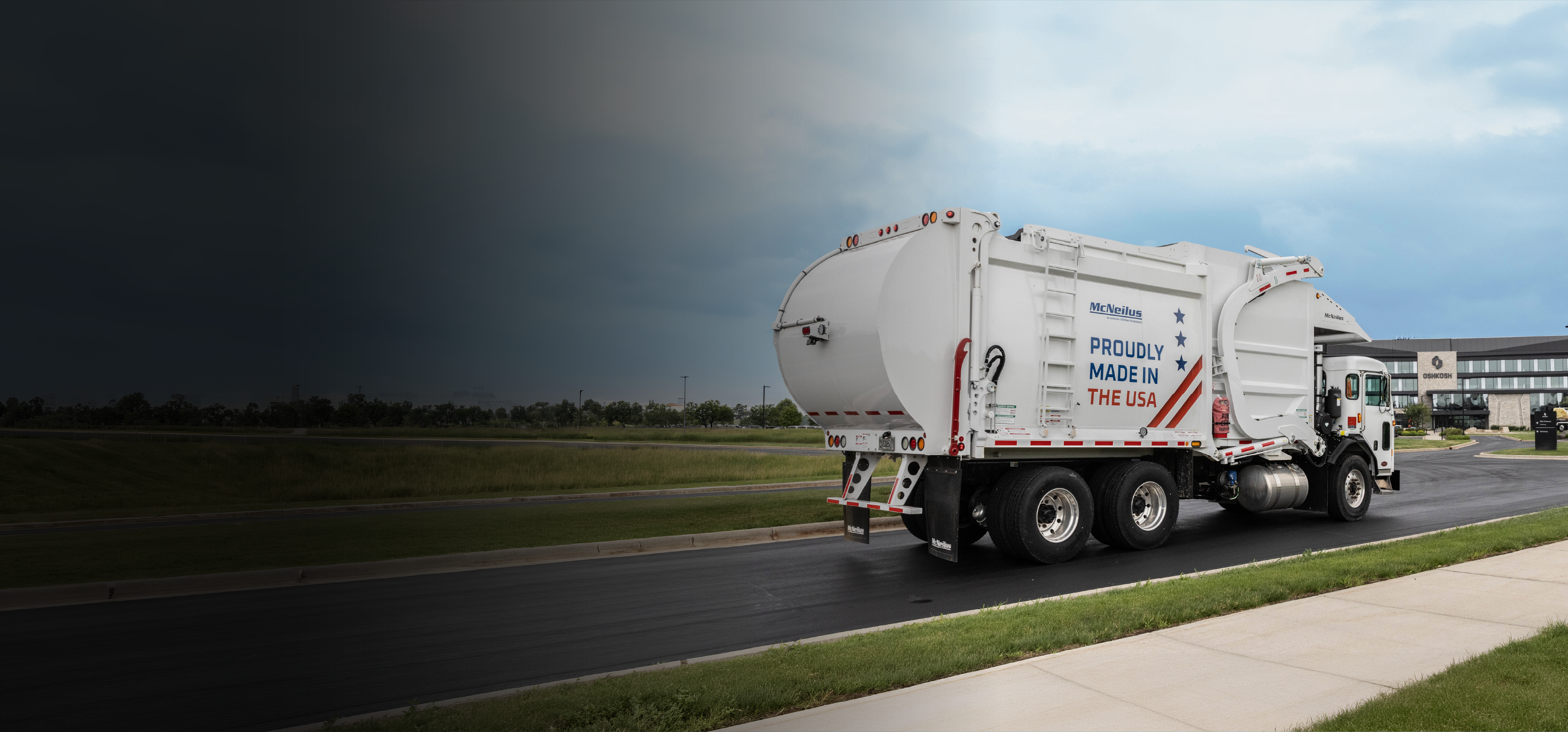 White McNeilus front loader refuse and recycling truck with red, white and blue graphics driving in front of Oshkosh global headquarters